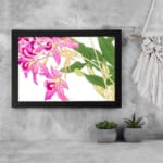 Vintage floral wall art with pink orchids, yellow centers, green leaves, and a black frame on a white background. displayed on the wall