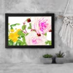 Vintage floral wall art with pink and white roses, red buds, and green leaves in a black frame on a white background. displayed on the wall