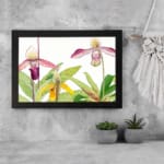 Vintage orchid wall art featuring purple, pink, and yellow flowers with green leaves on a white background. displayed on the wall in a black frame