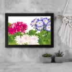 Vintage floral wall art with pink, white, and blue flowers surrounded by green leaves on a white background, framed in black for an elegant look. displayed on the wall