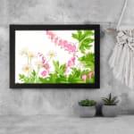 Vintage floral wall art with delicate pink and white flowers, green leaves, and a black frame on a white background. displayed on the wall