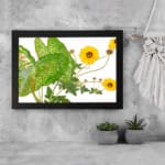 Vintage floral wall art with bright yellow flowers, green leaves, and a black frame on a white background. displayed on the wall