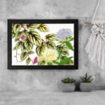 Vintage floral wall art with soft yellow and light purple flowers, green leaves with dark veins, and a white background. displayed on the wall in a black frame