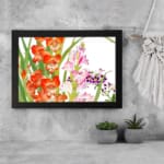 Vintage floral wall art with bright orange and soft pink flowers, green leaves, and a black frame on a white background. displayed on the wall