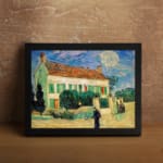 Infidu vintage wall art featuring a house with a red roof, green shutters, and a bright blue sky with the sun or moon shining, surrounded by lush grass and a walking path. displayed on the wall art in a black frame