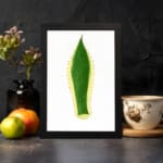 Minimalist green leaf design with yellow outline and dotted edges on white background, framed in black, vintage wall art. displayed on the wall in a black frame