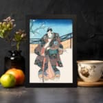 Vintage wall art of a Japanese samurai in a floral kimono standing in a peaceful winter scene with a snowy backdrop and a tree branch. displayed on the wall in a black frame
