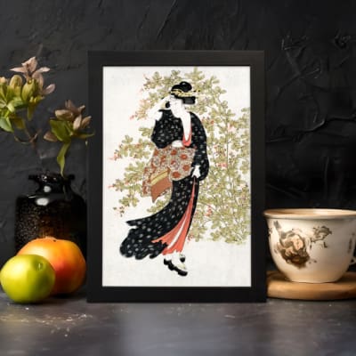 Vintage wall art of a Japanese woman in a black kimono holding a fan, with delicate trees in the background. displayed on the wall in a black frame