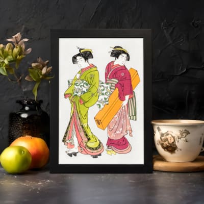 Two Japanese women in traditional green and red kimonos with decorative items, illustrated in elegant vintage style. displayed on the wall in a black frame