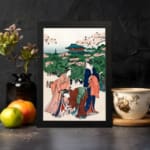 Vintage Japanese wall art of women in kimonos under cherry blossom trees with a temple in the background. displayed on the wall in a black frame