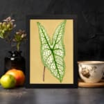 Vintage botanical wall art showing a detailed green leaf with bold veins on a soft beige background. displayed on the wall in a black frame