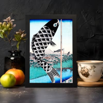 Infidu vintage wall art featuring a black koi fish hanging on a pole with intricate scales, set against a traditional Japanese landscape with a blue sky, serene water, and a classic bridge. displayed on the wall art in a black frame