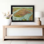 Vintage aerial view of a historic waterfront city with detailed buildings, boats, and earthy tones. displayed on the wall in a black frame
