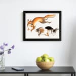 Vintage wall art of a fox and two rabbits in motion, hand-drawn in natural colors with a clean white background. displayed on the wall in a black frame