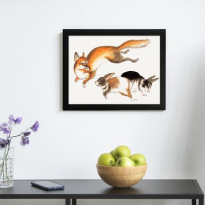 Vintage wall art of a fox and two rabbits in motion, hand-drawn in natural colors with a clean white background. displayed on the wall in a black frame