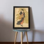 Vintage Japanese wall art of a woman in a kimono with floral patterns, set against a soft green and beige background. displayed on the table in a black frame