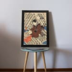Vintage Japanese ukiyo-e wall art of a scholar writing on a scroll, with intricate calligraphy in the background. displayed on the table in a black frame