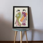 Vintage Japanese wall art with two women in kimonos, detailed patterns, and soft, rich colors. displayed on the table in a black frame