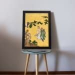 Vintage Asian wall art with two figures in traditional robes under a pine tree, set against a golden background with delicate brushwork. displayed on the table