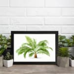 Vintage wall art with a detailed green palm plant in a black frame, featuring bright green leaves and a white background for a fresh, elegant look. displayed on the wall
