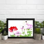 Vintage floral wall art with red, purple & white flowers, green leaves, and a black frame on a white background. displayed on the wall
