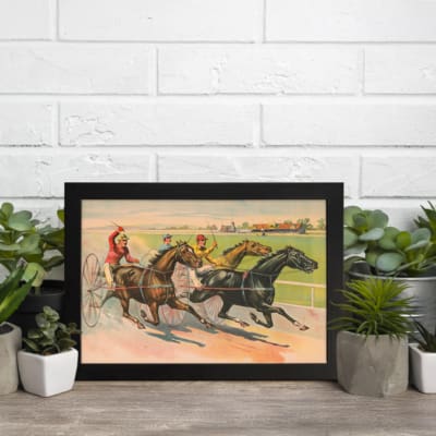 Vintage horse racing wall art with jockeys riding on a dirt track, surrounded by a countryside landscape with a farmhouse, framed in black. displayed on the wall