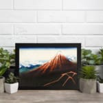 Vintage mountain landscape wall art with red, brown, and blue tones, featuring a striking reddish-brown mountain, blue sky, and black frame. displayed on the wall