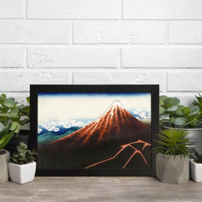 Vintage mountain landscape wall art with red, brown, and blue tones, featuring a striking reddish-brown mountain, blue sky, and black frame. displayed on the wall