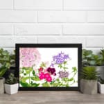 Infidu Vintage Floral Wall Art with soft pink, purple, and deep red flowers, green leaves, and a white background for a timeless, elegant look. displayed on the wall in a black frame