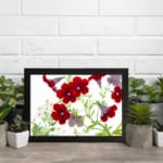 Vintage floral wall art with red and purple trumpet flowers, green leaves, and a black frame on a white background. displayed on the wall