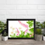 Vintage floral wall art with delicate pink and white flowers, green leaves, and a black frame on a white background. displayed on the wall