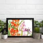 Vintage floral wall art with bright orange and soft pink flowers, green leaves, and a black frame on a white background. displayed on the wall
