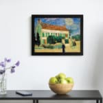 Infidu vintage wall art featuring a house with a red roof, green shutters, and a bright blue sky with the sun or moon shining, surrounded by lush grass and a walking path. displayed on the wall art in a black frame