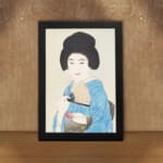 Vintage art of a Japanese woman in a light blue kimono holding a fan with a calm expression and soft background. displayed on the wall in a black frame
