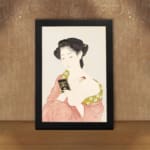 Vintage Japanese wall art featuring a woman in traditional dress holding a book with soft red and green patterns. displayed on the wall in a black frame