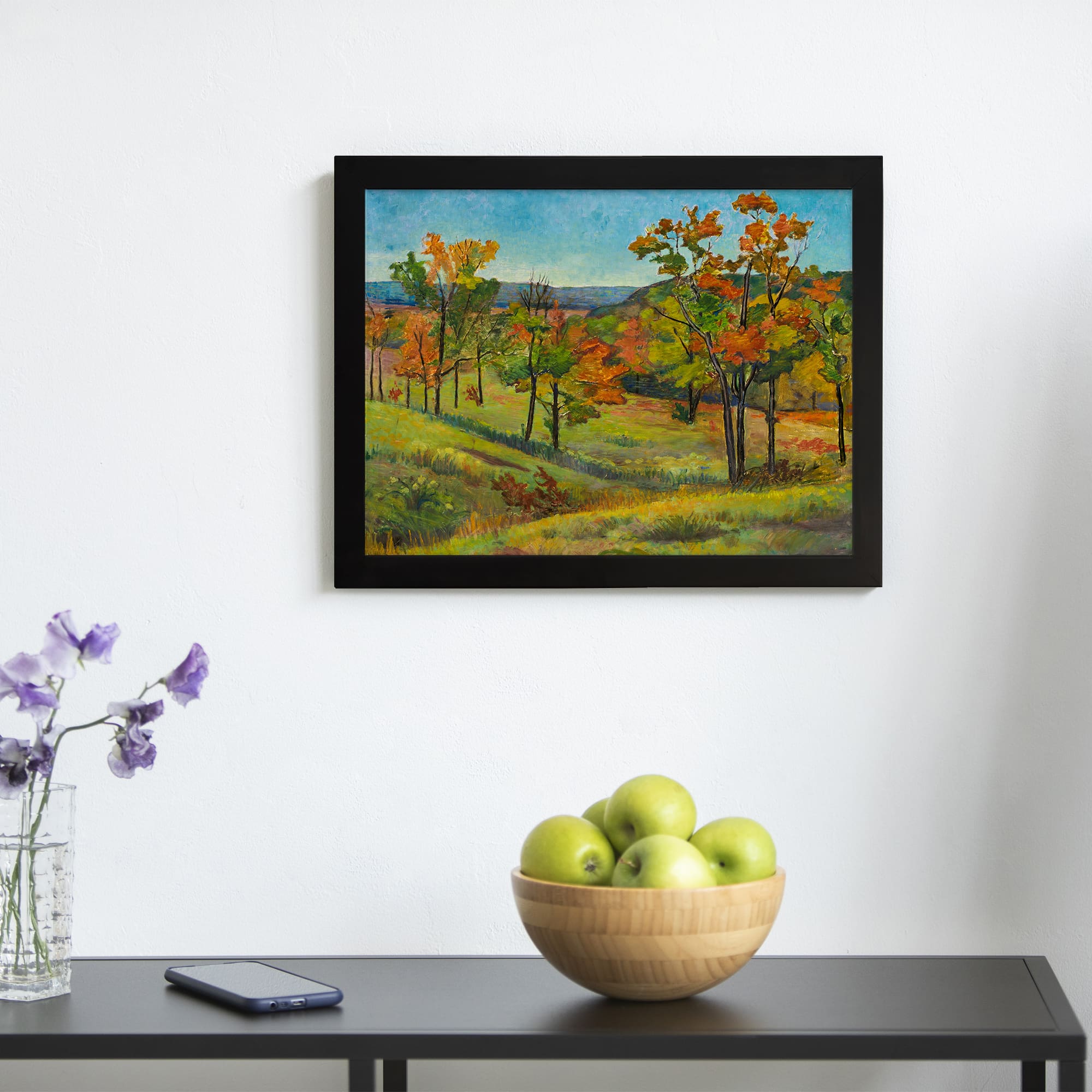 Vintage wall art of a colorful autumn landscape with trees in red, orange, and yellow displayed on the wall in a black frame