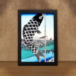 Infidu vintage wall art featuring a black koi fish hanging on a pole with intricate scales, set against a traditional Japanese landscape with a blue sky, serene water, and a classic bridge. displayed on the wall art in a black frame