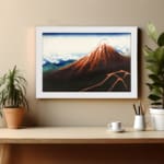 Vintage mountain landscape wall art with red, brown, and blue tones, featuring a striking reddish-brown mountain, blue sky, and white frame. displayed on the wall