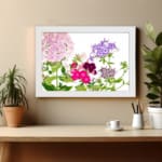 Infidu Vintage Floral Wall Art with soft pink, purple, and deep red flowers, green leaves, and a white background for a timeless, elegant look. displayed on the wall in a white frame