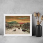 Infidu vintage wall art of a winter scene with horse-drawn sleighs passing through a snowy town, featuring warm sky tones and a peaceful landscape. displayed on the wall art in a white frame