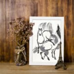 Infidu vintage wall art featuring two horses in black and white ink with bold brushstrokes, creating a timeless and dynamic design. displayed on the wall art in a white frame