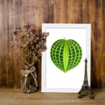Heart-shaped green leaf with light and dark green patterns on a white background, framed in white, vintage botanical wall art displayed on the wall
