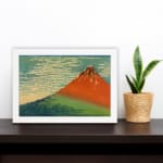 Infidu vintage wall art featuring an iconic view of Mount Fuji with a red-orange peak, a blue sky, and lush green surroundings in a traditional Japanese style. displayed on the wall art in a white frame