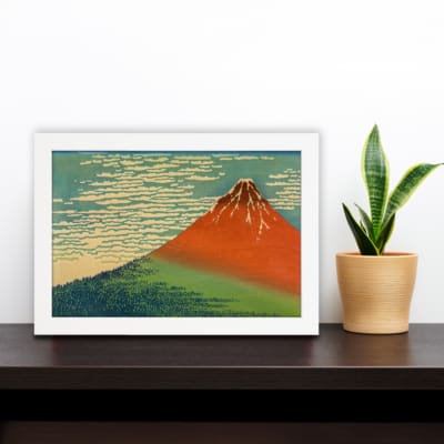 Infidu vintage wall art featuring an iconic view of Mount Fuji with a red-orange peak, a blue sky, and lush green surroundings in a traditional Japanese style. displayed on the wall art in a white frame