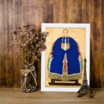 Vintage wall art of a classic East Asian portrait showing a person in a royal blue robe with gold accents on a beige background. displayed on the wall in a white frame