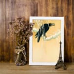 Infidu vintage wall art featuring a black crow perched on a snow-covered tree against a soft beige or light golden background, creating a timeless and artistic winter scene. displayed on the wall art in a white frame