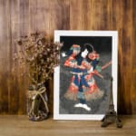 Japanese figure in bold red and blue kimono striking a dramatic pose against a dark vintage-style background. displayed on the wall in a white frame
