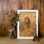 Vintage wall art of a majestic lion family in a natural setting with warm earthy tones, including a lion, lioness, and cubs in a savannah backdrop. displayed on the wall in a white frame
