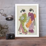 Vintage Japanese wall art with two women in kimonos, detailed patterns, and soft, rich colors. displayed on the wall in a white frame