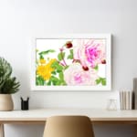 Vintage floral wall art with pink and white roses, red buds, and green leaves in a white frame on a white background. displayed on the wall